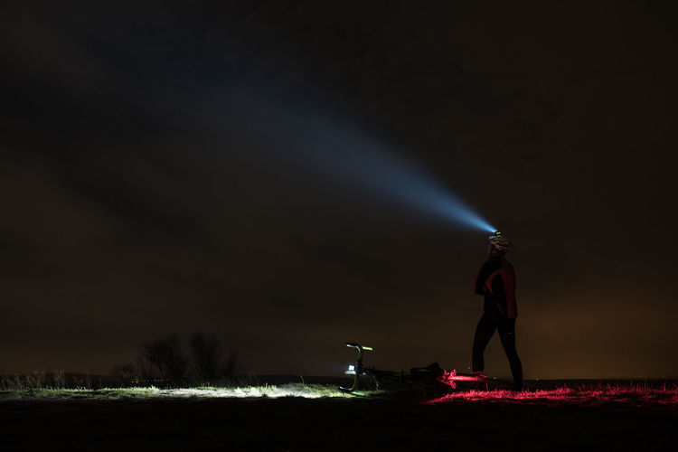 Man with headlamp standing on field against sky at night