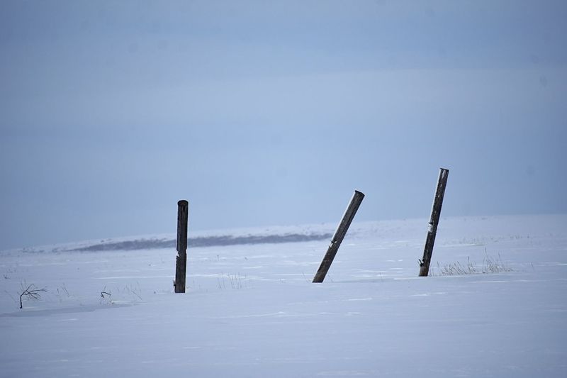 Wooden posts on snow covered field against sky