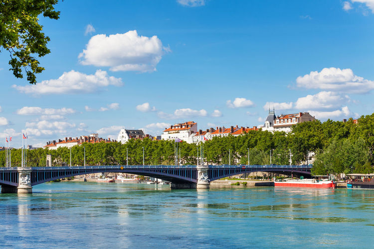 Bridge over river by buildings against sky