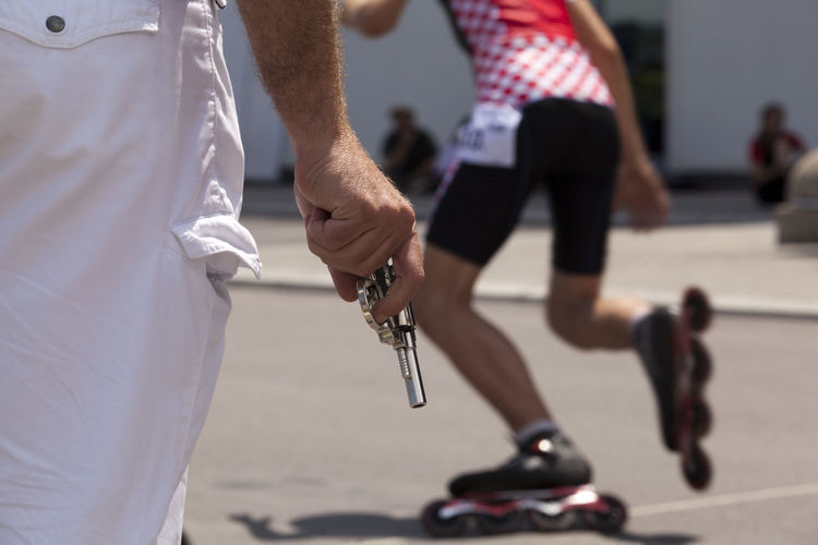 Midsection of man holding gun by inline skater during competition