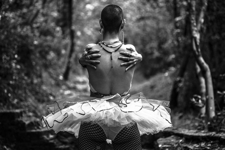 Rear view of shirtless young woman dancing in forest