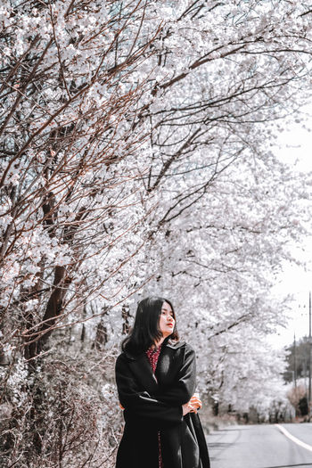 Full length of woman standing by cherry tree in winter