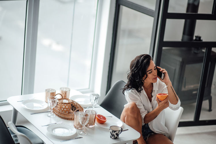 Woman eating fruit while talking over smart phone while sitting on chair at home