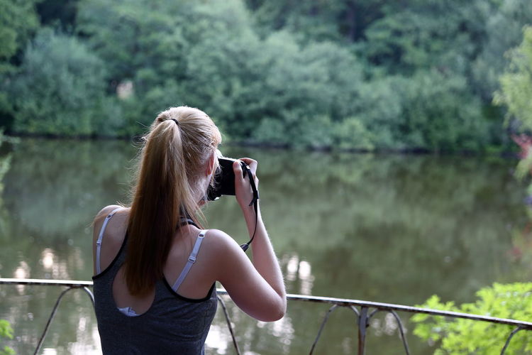 Rear view of woman photographing by lake