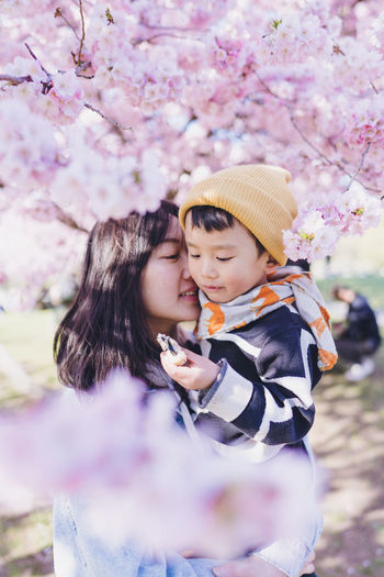 A mom held her son in her arms standing in pink sakura blossom. it was a spring in munich, germany. 