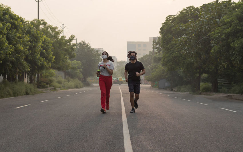 Full length of couple wearing masks running on road in city