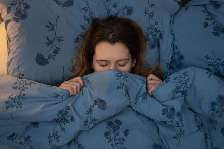 Attractive young caucasian girl sleeping in bed. woman wrapped up in a blanket up to her nose.