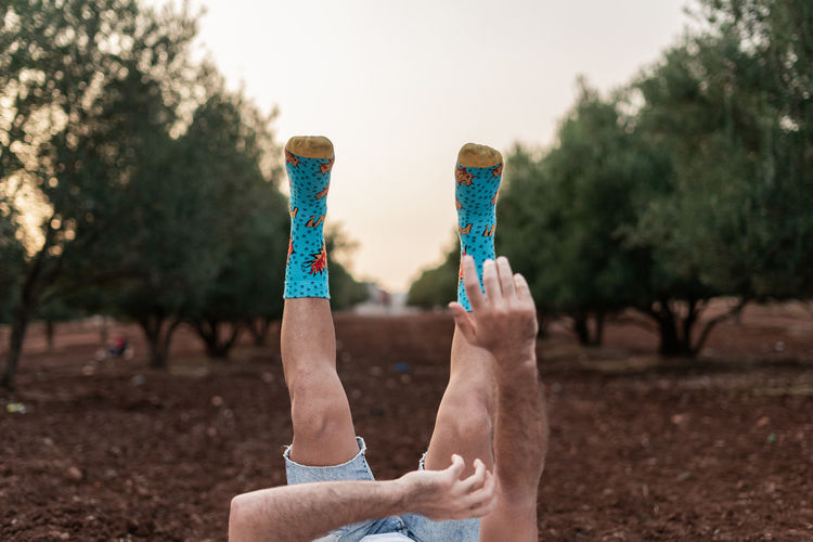 Man's legs and blurry hands up in the air with colourful socks and blue jeans short.