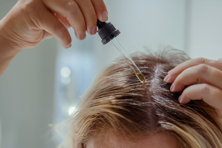 Woman applies oil to her hair with pipette. beauty caring for scalp and hair.