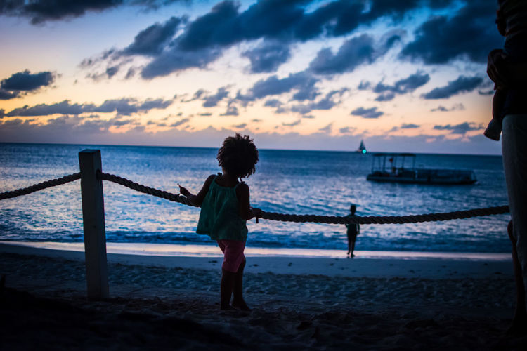 Girl standing at beach against sky during sunset