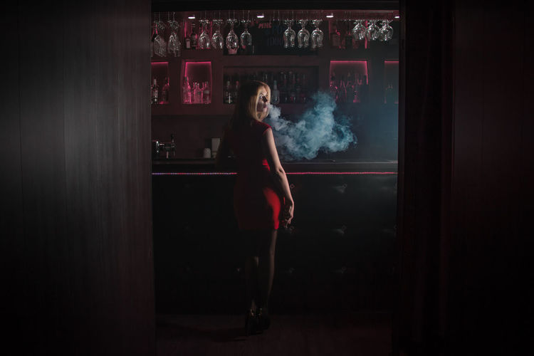 Rear view of young woman smoking at bar counter
