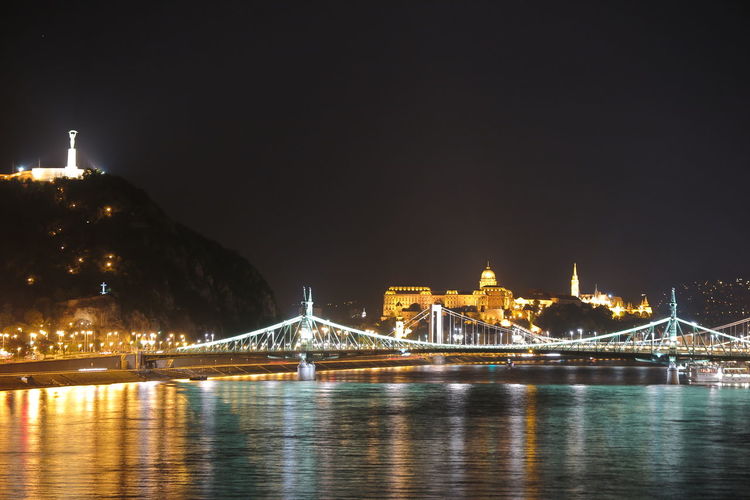 Illuminated freedom bridge in budapest over the river danube at night with gellert and buda hills 