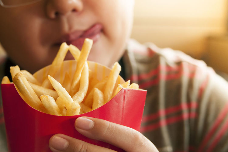 Cropped image of tempted boy holding french fries packet