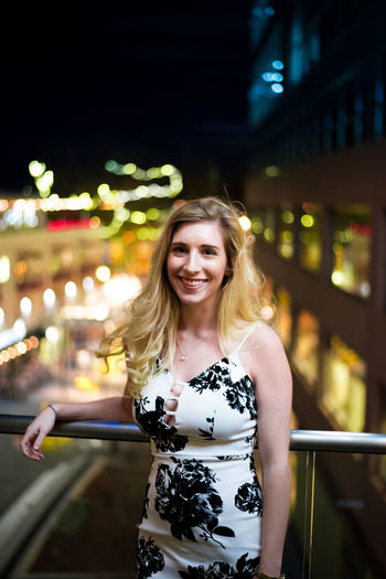 Portrait of smiling young woman standing in balcony at illuminated city