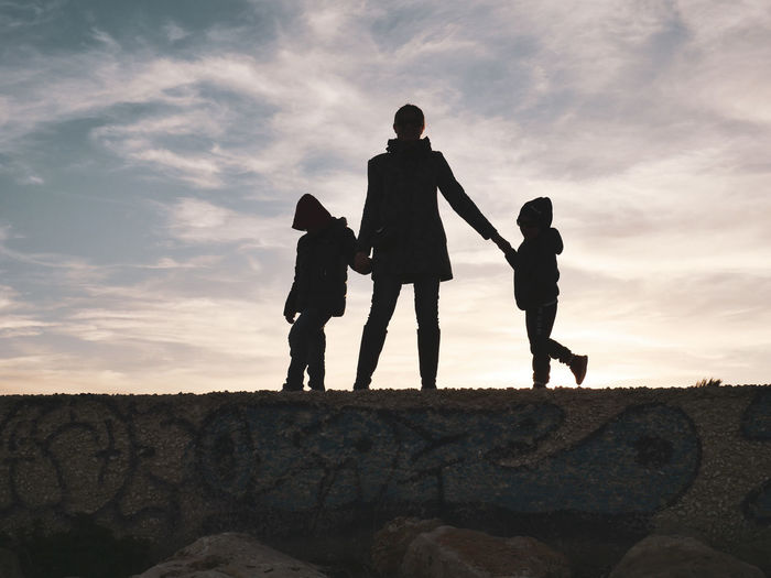 Silhouette mother with children standing against sky during sunset