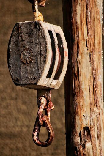 Close-up of rusty pulley hanging from wooden post