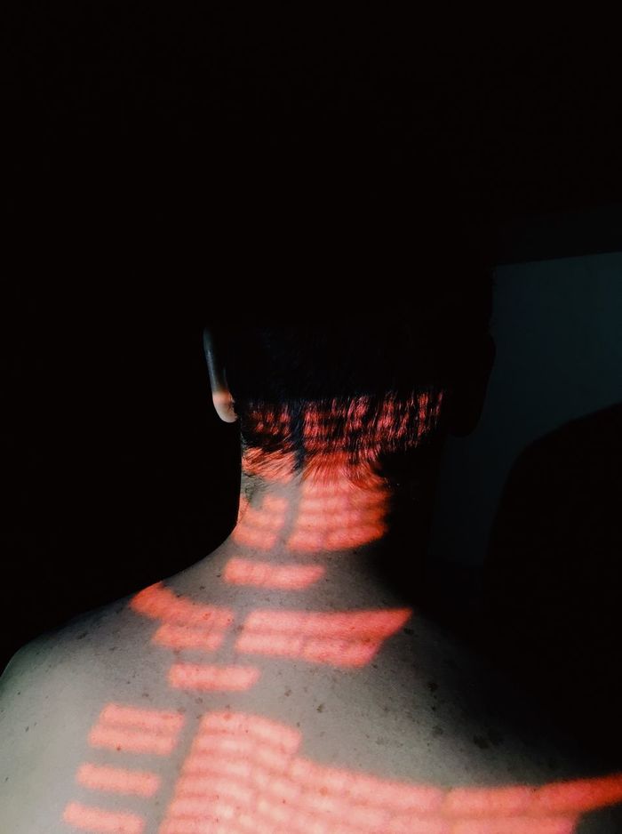 Rear view of shirtless man with red lights against black background