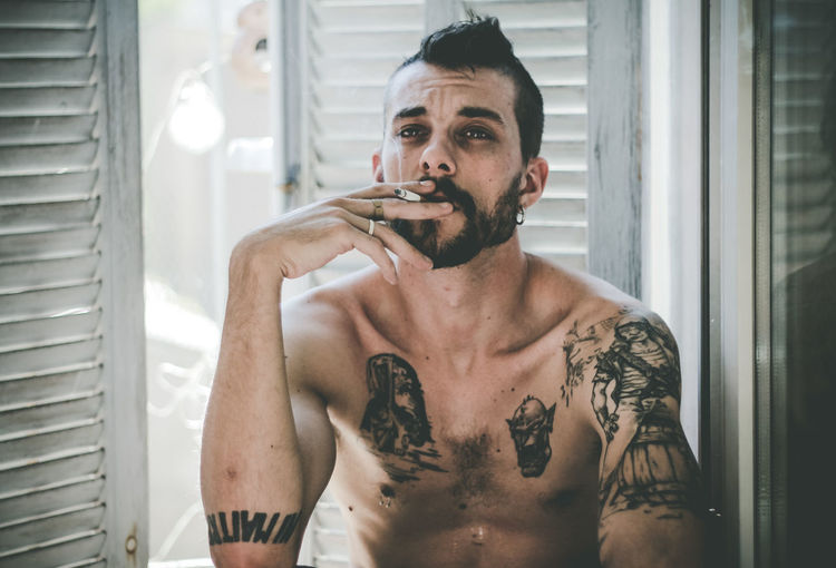 Close-up of shirtless man smoking cigarette at home