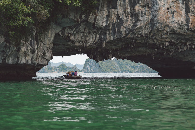 People rowing boat on halong bay under rock formation