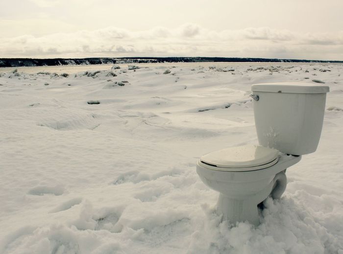 Toilet bowl on snow covered field against sky