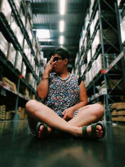 Full length of woman sitting amidst shelves