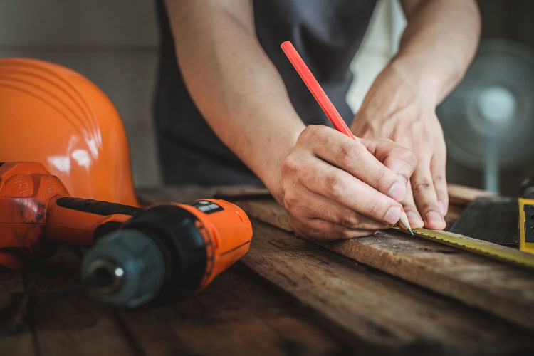 Midsection of male carpenter marking on wood in workshop