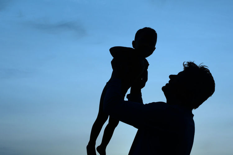 Low angle view of silhouette father lifting son against sky