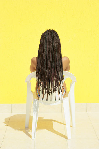 Rear view of woman sitting on chair against yellow wall
