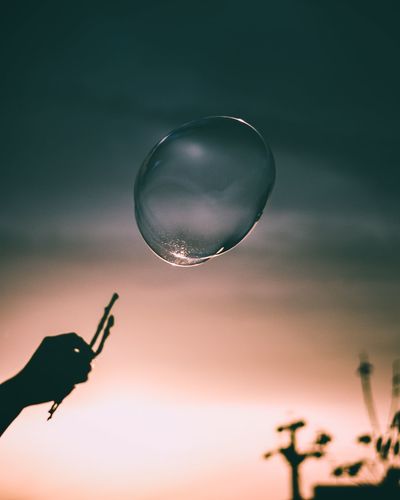 Cropped image of hand holding bubbles against sky