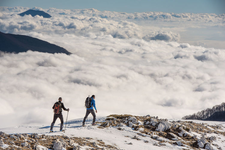 People hiking on snowcapped mountain against sky