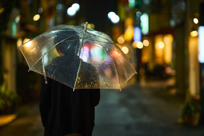 Rear view of person holding umbrella at night