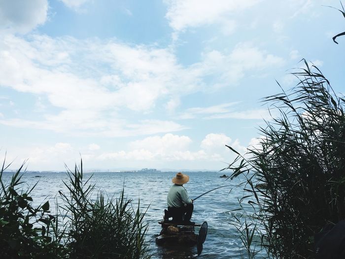 Rear view of man fishing while sitting on rocks in lake