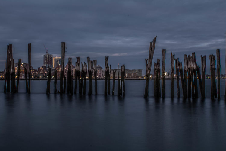 Wooden posts in sea against sky in city