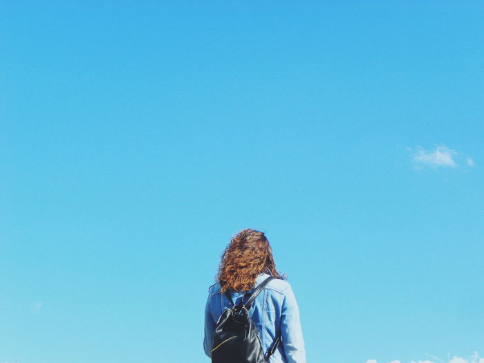 Rear view of mature woman with backpack standing against blue sky during sunny day