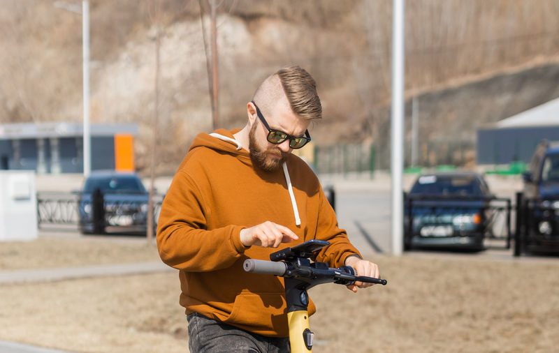 Man wearing sunglasses using mobile phone on push scooter