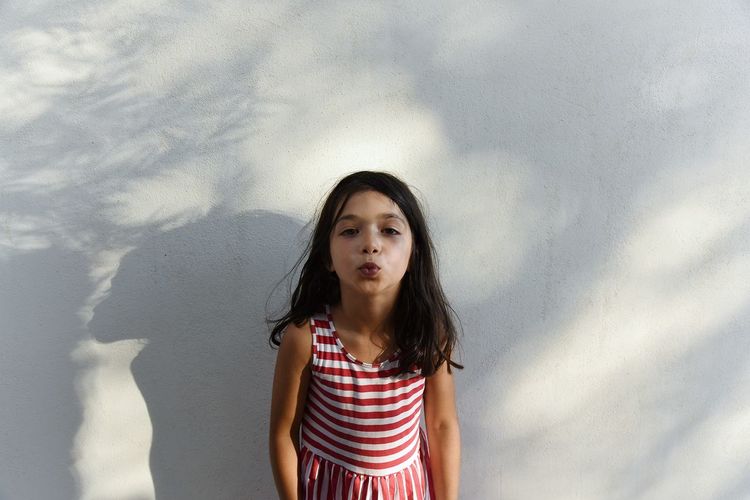 Portrait of girl puckering lips while standing against white wall