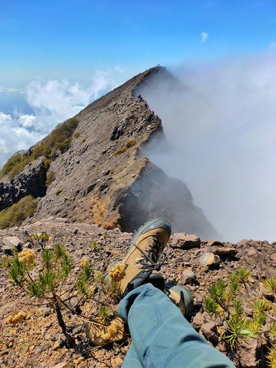 Low section of person sitting by mountain against sky
