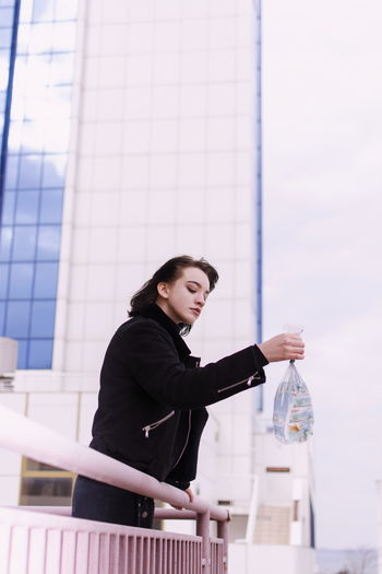 Girl holding fish in plastic bag while standing against building