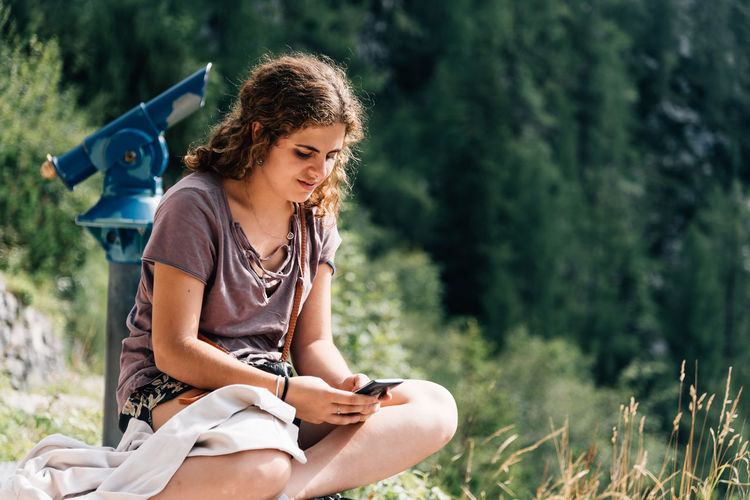 Young woman using mobile phone while sitting against tree