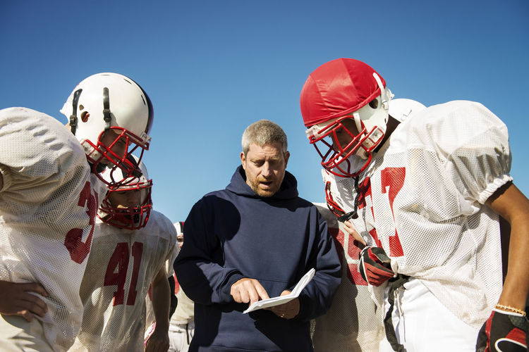 Coach sharing strategy to american football players standing on field