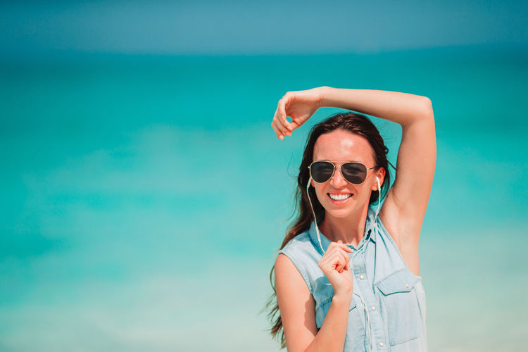 Cheerful woman listening music at beach