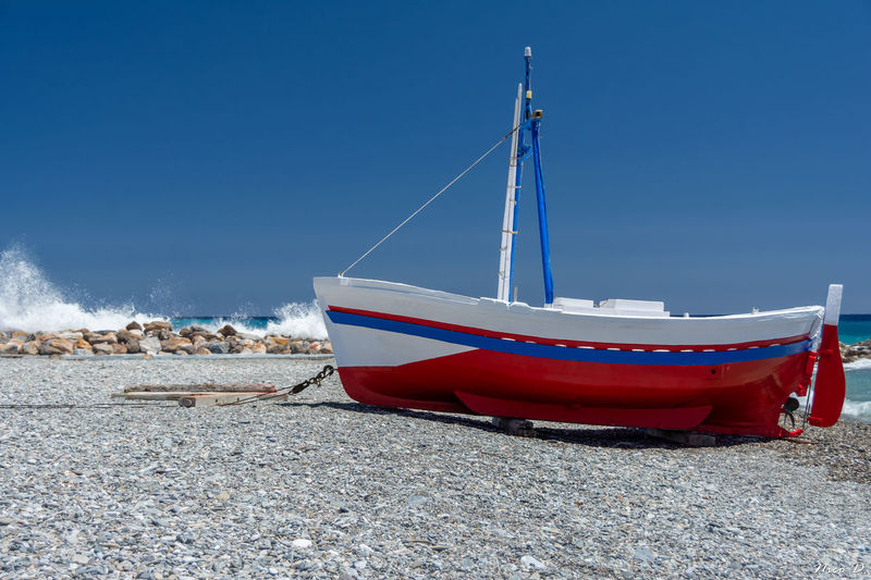Boat moored on beach against clear blue sky