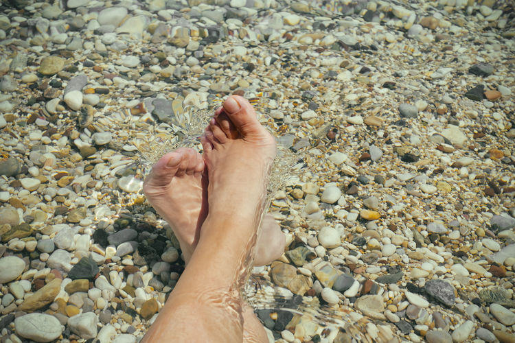 Low section of person legs on pebbles at beach