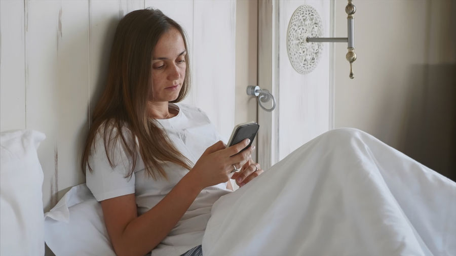Young woman using phone while sitting on bed