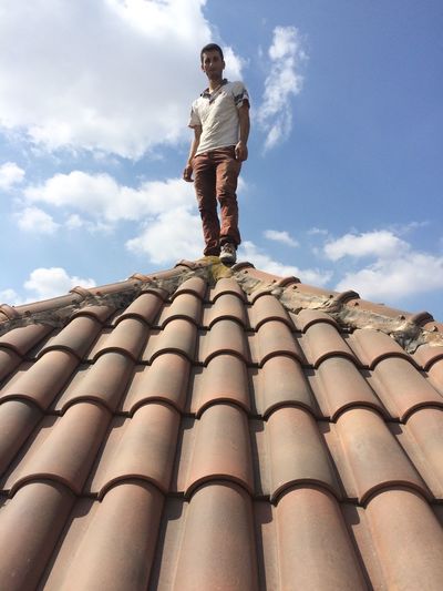 Low angle view of man standing on roof against sky