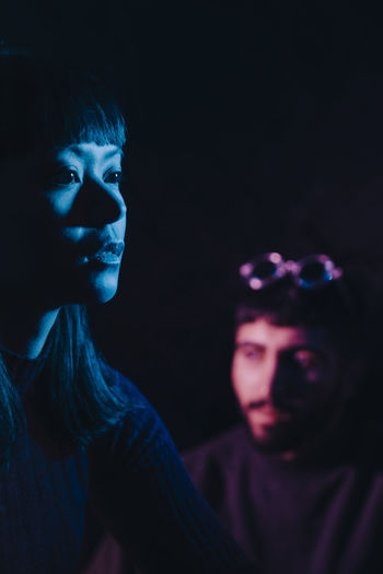 Thoughtful young woman sitting near male friend in dark at restaurant