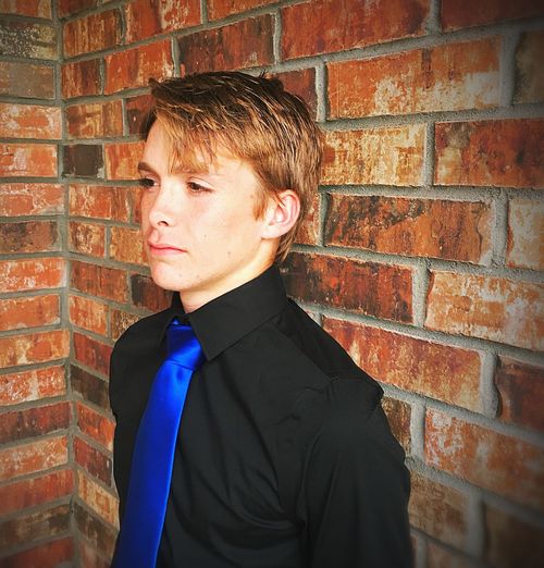 Teenage boy standing against brick wall