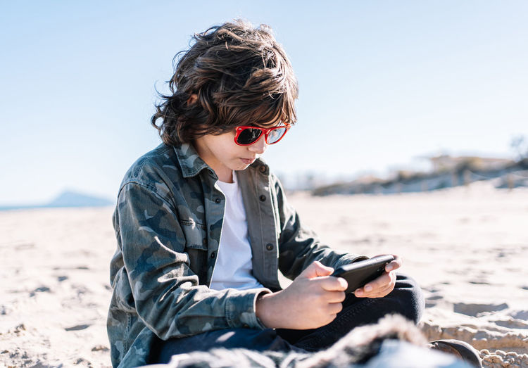Young woman using phone while sitting on beach
