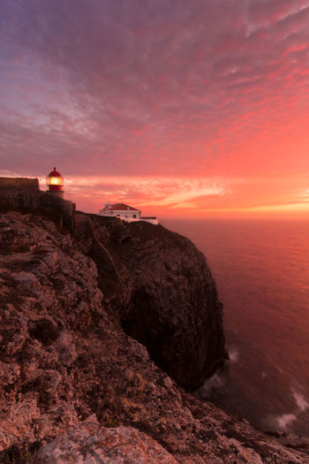 Coastline landscape at sunset with reddish sky and a lighthouse lit on the cape of san vicente, portugal