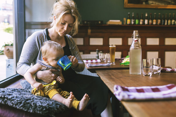 Mid adult woman feeding water to son in restaurant